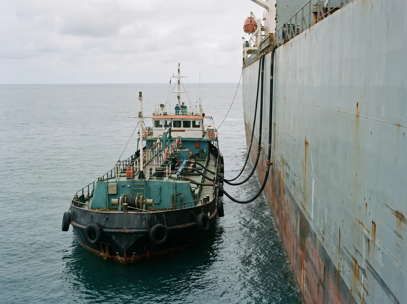 Bunker vessel alongside a freighter, hoses between the hulls