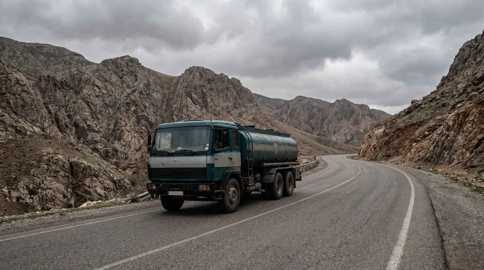 Tanker truck on a mountain road under a cloudy sky